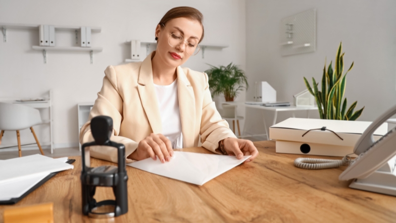 A woman prepares official documents at her desk with a notary stamp beside her, symbolizing the launch plan for becoming a notary in Ohio
