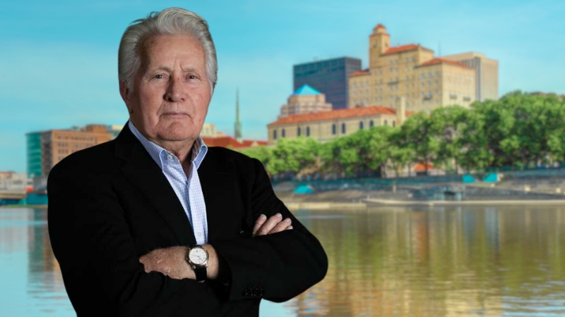 Martin Sheen stands in front of the Dayton skyline