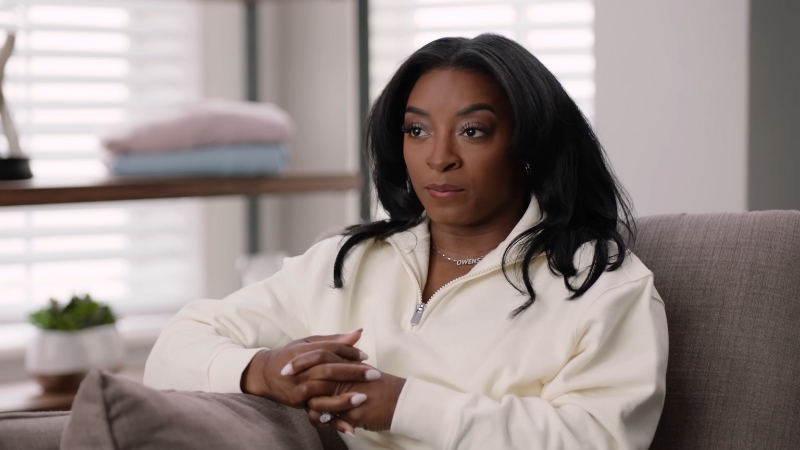 Simone Biles sits in a white sweater