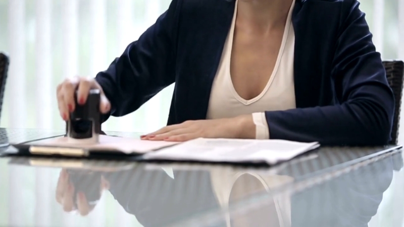 A woman in a business suit stamps official documents at a desk, representing the notary process in Ohio