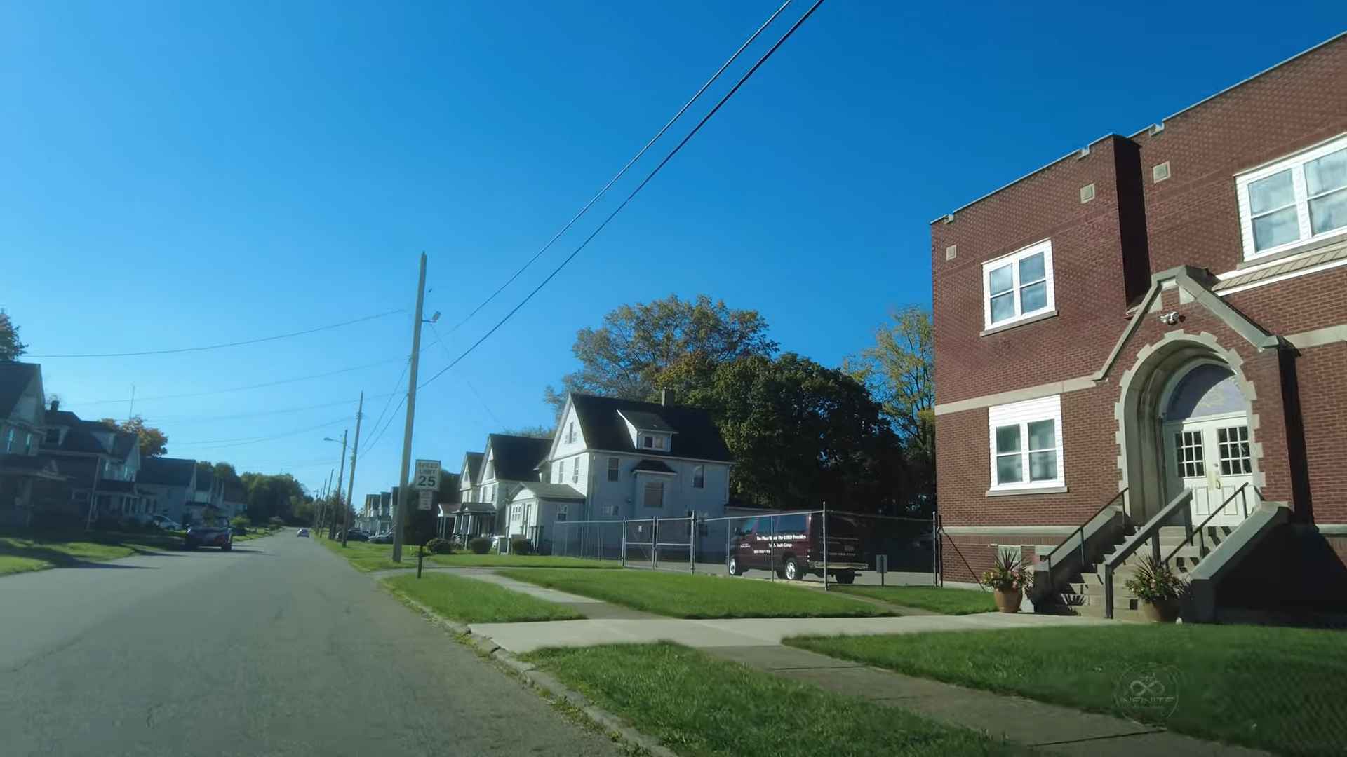 A quiet street in Youngstown, Ohio, with houses on the left and a red brick building on the right under a clear blue sky
