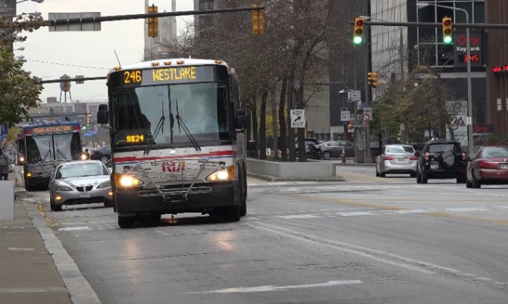 A bus driving down a street in Cleveland, passing traffic lights with vehicles in the background